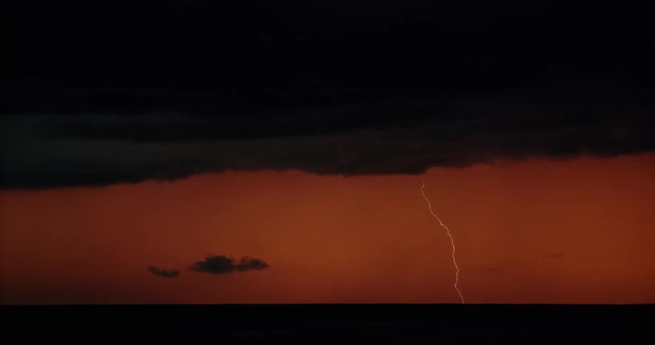 Lightning streaking arcs flashing over the silhouette of black clouds on a red sky