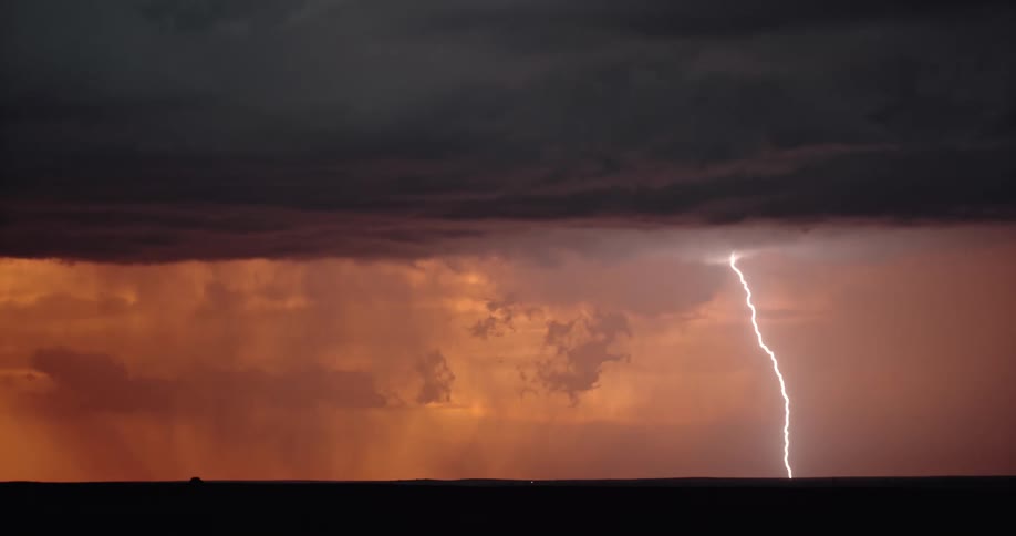 An enormous bolt of lightning descends from a dark storm cloud hovering above an orange sky