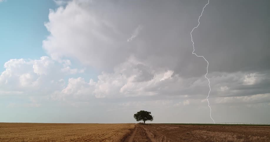 Lightning flashing in a cloudy sky over a rural field in the daytime