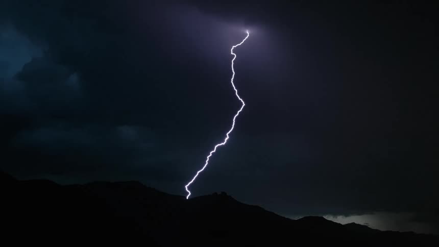 Lightning bolts flash and branch out in the dark sky above a mountain range