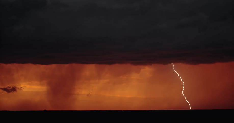 Lightning flashes between an orange sky thick with dark clouds and vast field shrouded in shadow