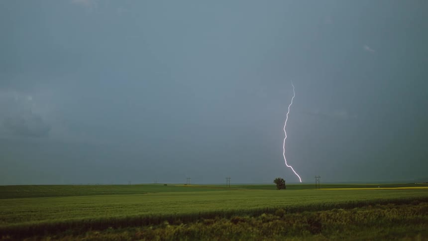 Lightning streaking arcs flashing across storm clouds hitting the ground over a field