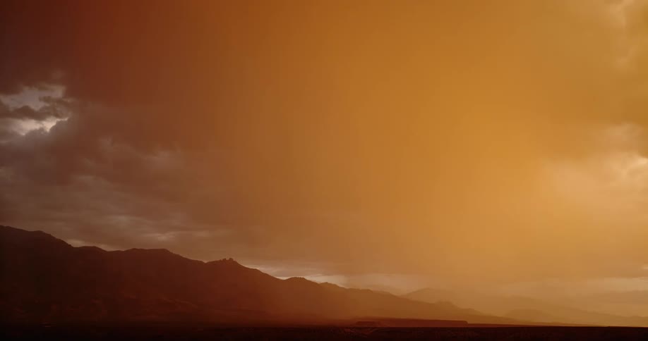 Lightning strikes across the sky in the distance behind clouds in an orange sky next to a mountain range