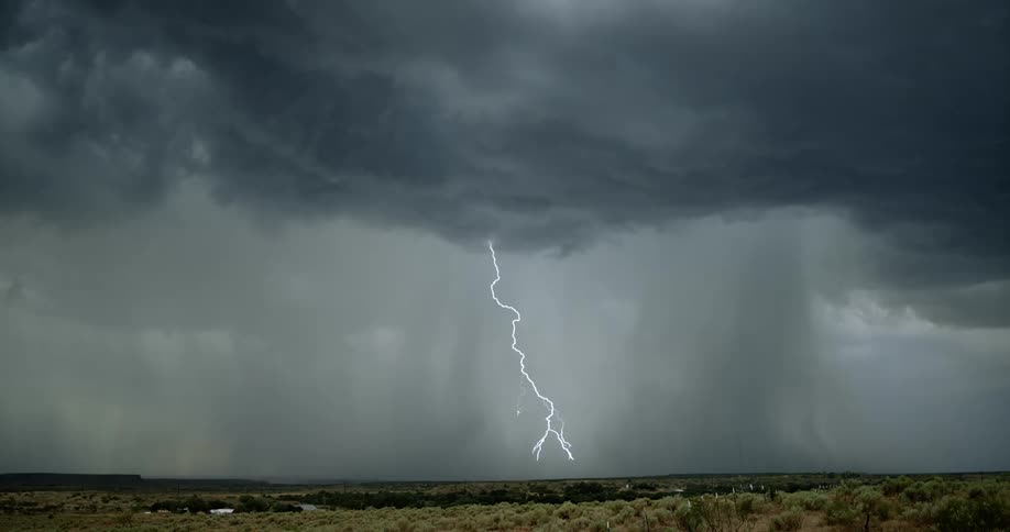 Many bolts of lightning strike the ground beneath ominously huge storm clouds as rain pours down