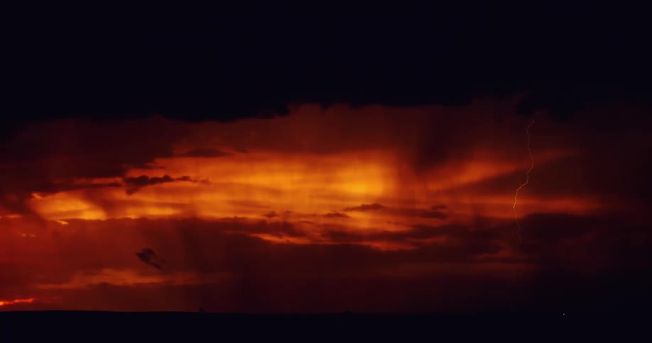 Lightning flashes across an orange glowing sky striking land