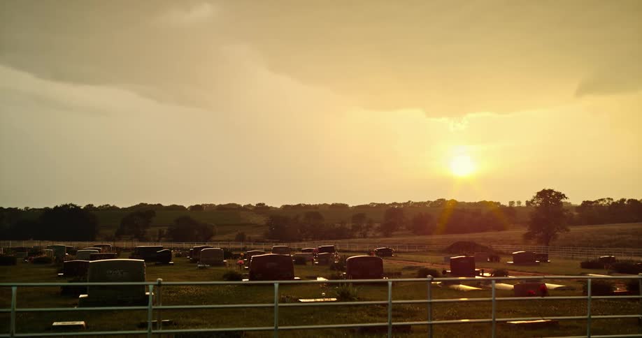 A cemetery with medium sized tombstones surrounded by a low metal fence at sunset