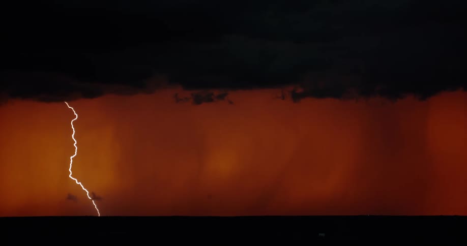 Lightning strikes down to the ground from a set of dark storm clouds in the evening