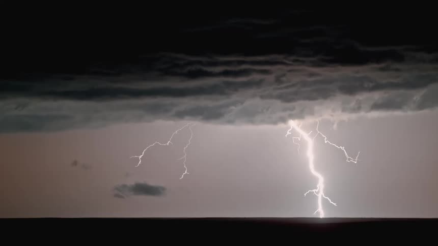 Lightning streaking arcs flashing across storm clouds hitting the ground over a field