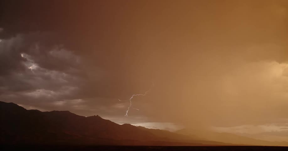 Lightning bolt comes down near mountains under an orange stormy sky