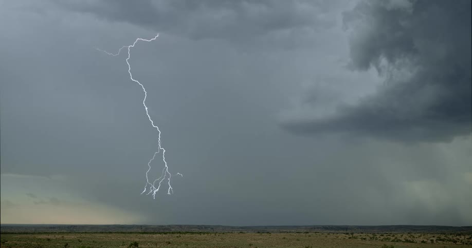 A flash of lightning streaks across the dark sky and down towards a field of grass