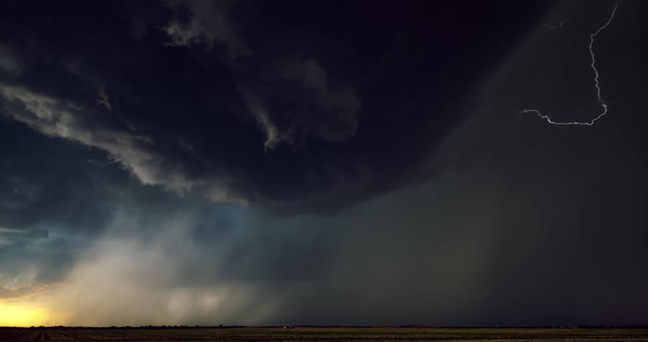 Dark storm cloud with lightning flashing around it and the sun on the horizon