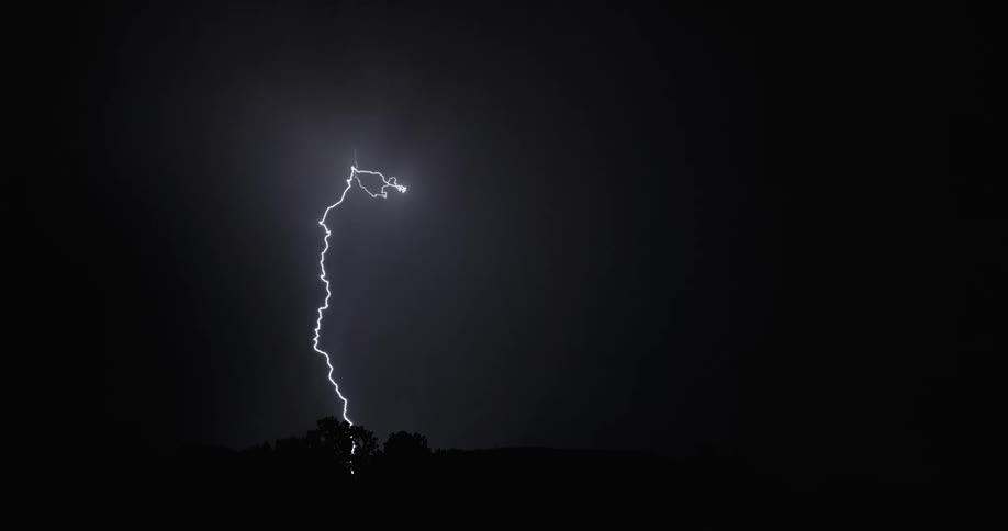 Veins of lightning flash in the night sky over the countryside during a thunderstorm