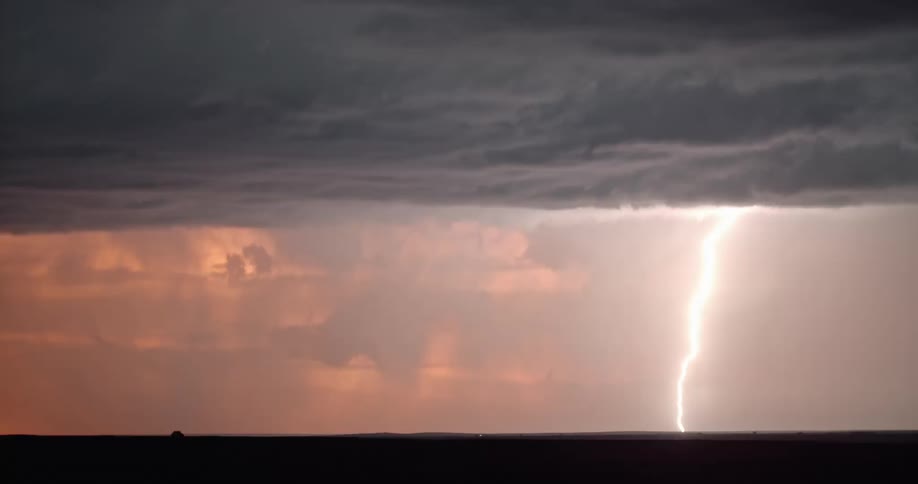 Lightning streaking arcs flashing across storm clouds over a field on a red sky