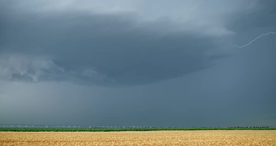 Lightning strikes over the sky and then down in the distance over a grass field at daytime