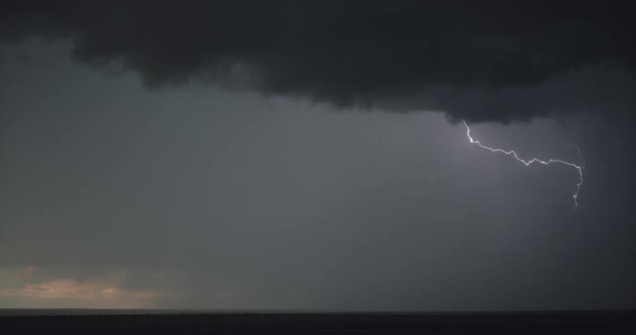 Lightning strikes flash towards the ground from dark clouds of a grassland in the evening