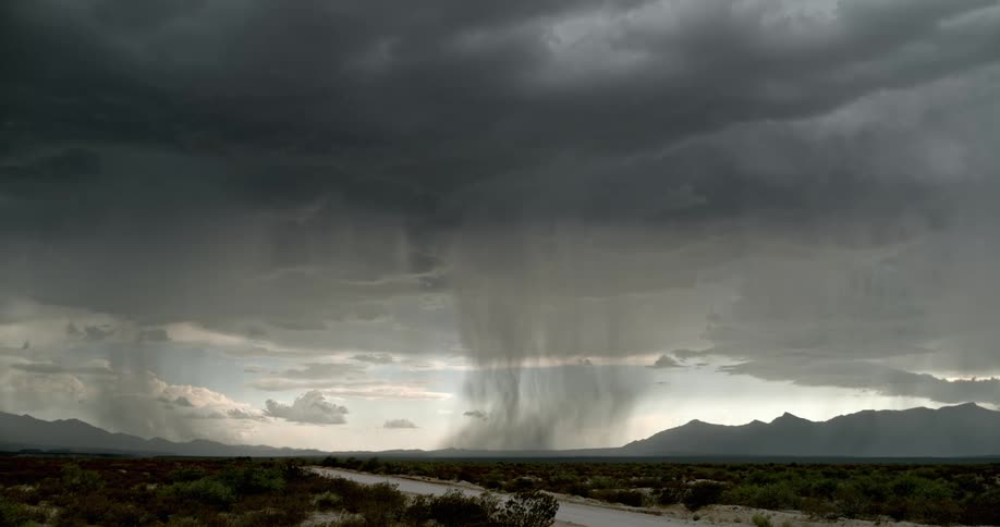 A flash of lightning strikes down onto the ground from a set of dark clouds in a thunderstorm over a field