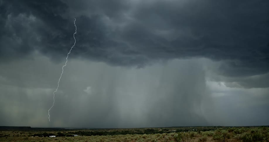 Lightning flashing in a cloudy sky during a rainstorm over a rural field