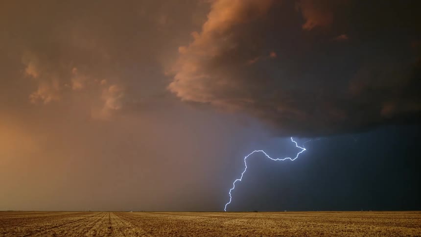 Lightning streaking arcs flashing accross yellow storm clouds over a field