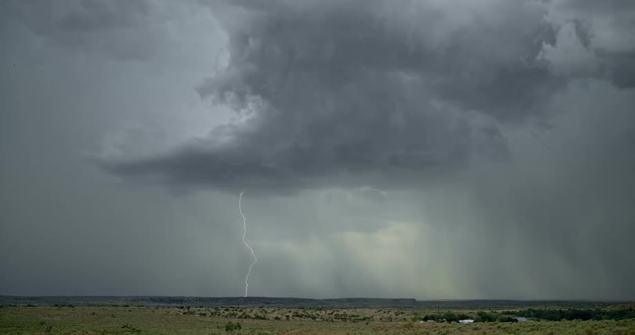 Lightning streaking arcs flashing accross storm clouds hitting the ground over a field