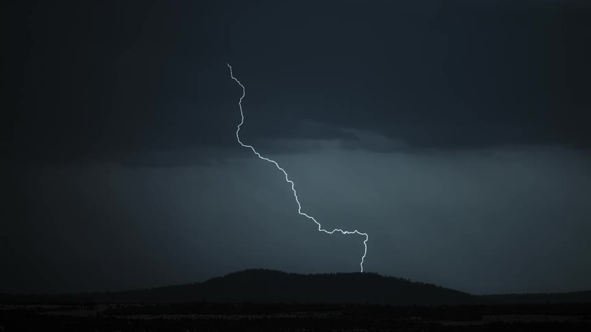 Lightning bolts from dark storm clouds flash over mountains and hit the ground