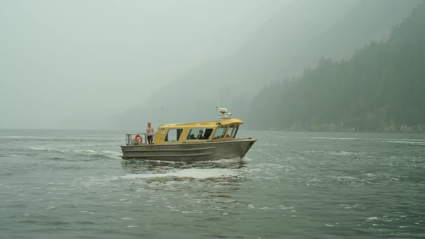 Small yellow boat arrives at the coast near the mist covered mountains