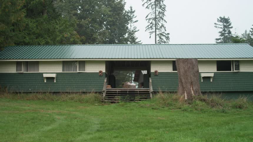 A front yard view of green and white house with a large doorway opening next to a tree stump at daytime
