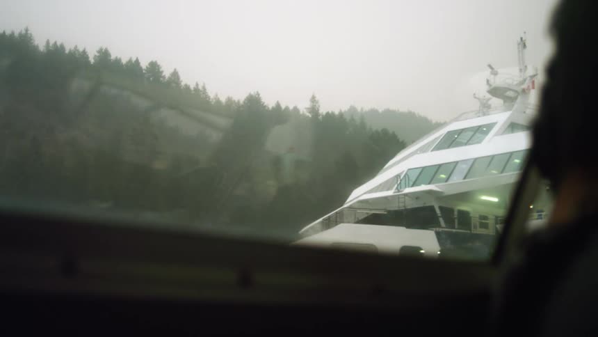 A vehicle with a window with a building trees the sky and clouds in the background