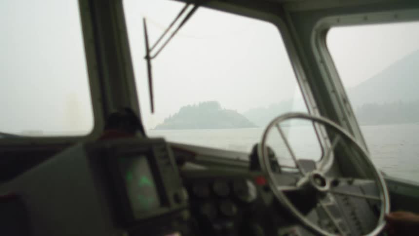 A person on the steering wheel of a small boat near the mountainous coast