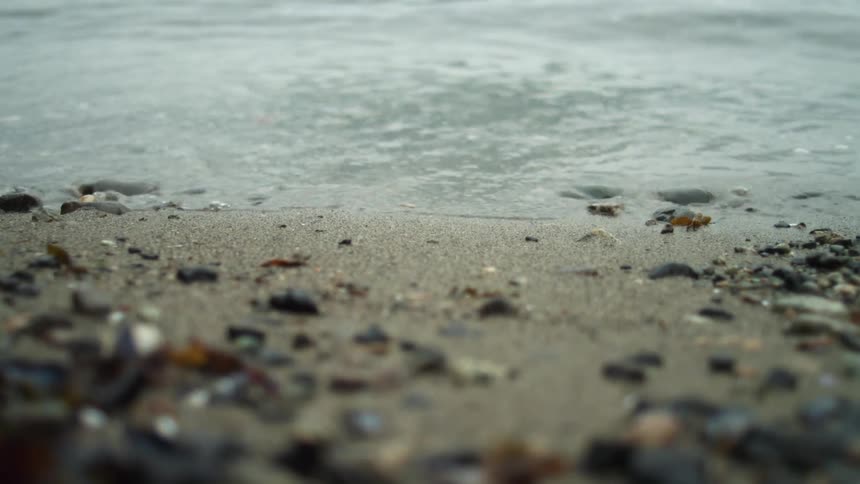 Calm small waves over the wet sand and pebbles in the coastal shoreline
