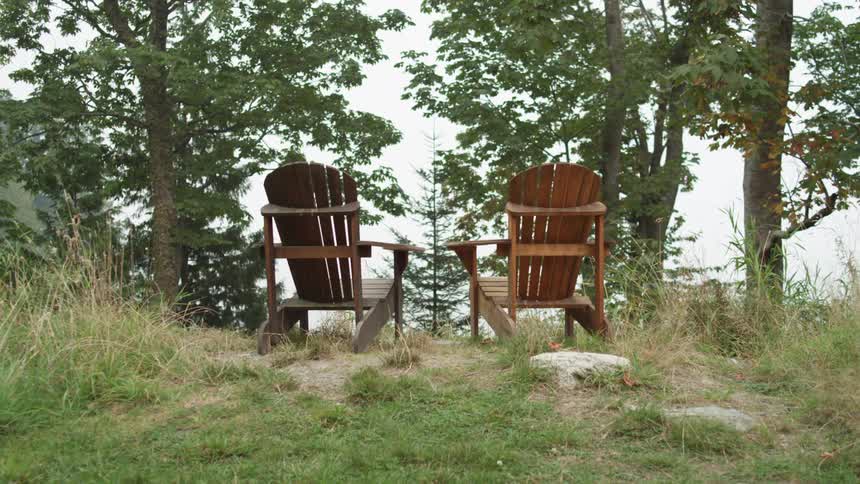 Two wooden lounge chairs outside on the edge of a slope in a forest at daytime