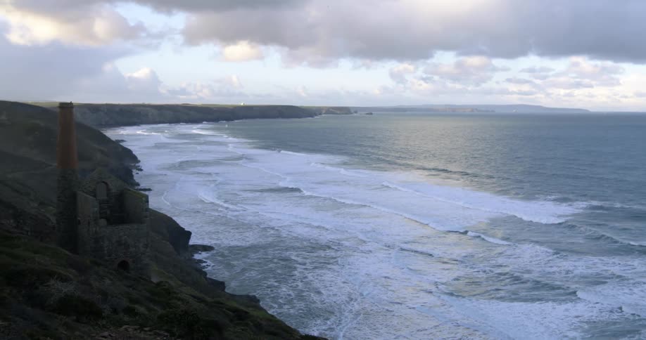 Ocean tides move in towards the shore of a small ocean side cliff at sunrise