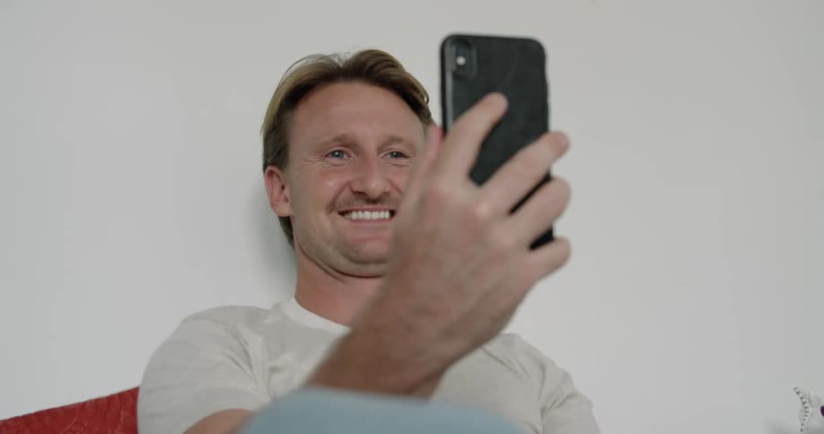 Man sitting in bed waves goodbye to someone on a video call on his smartphone