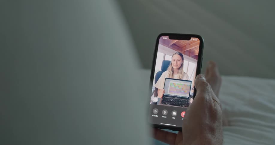 A young girl on a cell phone screen shows her laptop to the person holding the cell phone