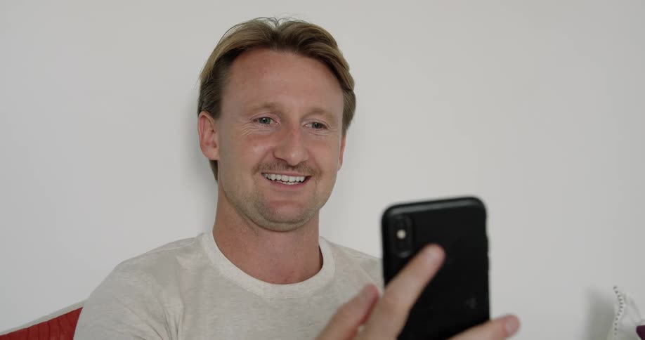 Man sitting in the living room greets someone on a video call through his smartphone