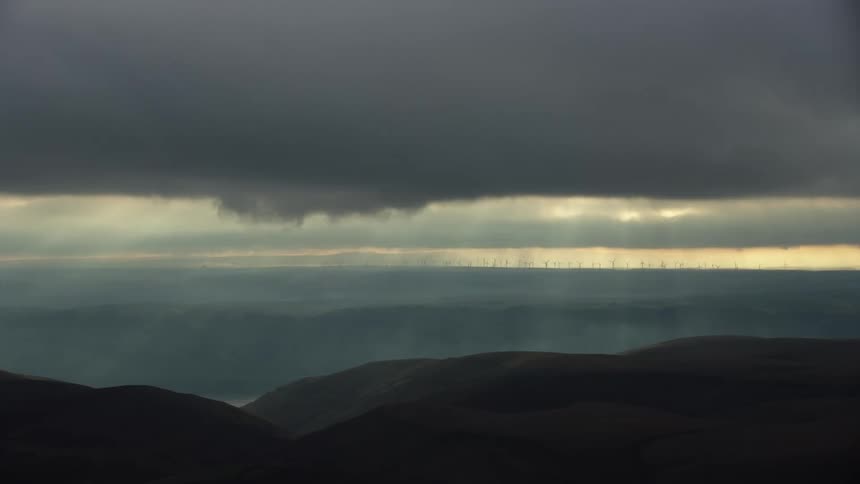 God rays stream down into the vast canyon below as many wind mills can be seen in the far horizon generating clean renewable energy