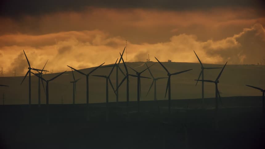 Aerial shot at sunset of a large wind farm with only a couple wind turbines rotating with many layers of clouds in the background