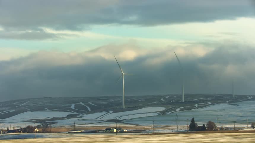 Wind turbines on the slope of a hill in a rural area with houses down below early one winter morning as they generate clean energy for rural and city electric utilities