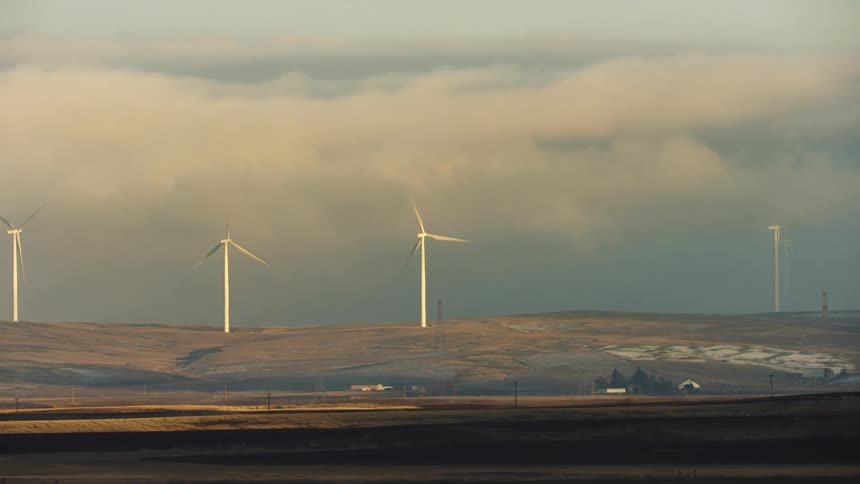 Looking across a broad rural farm valley as tall windmills rotate creating clean green energy in rural America