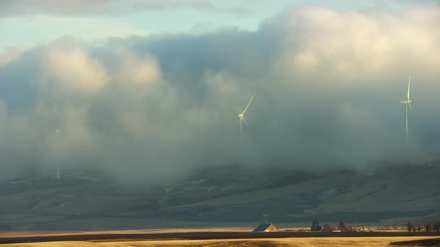 Slow zoom out reveal of wind turbines rotating in stormy winter clouds in a rural farm valley communicating green energy is being generated in any weather at all times