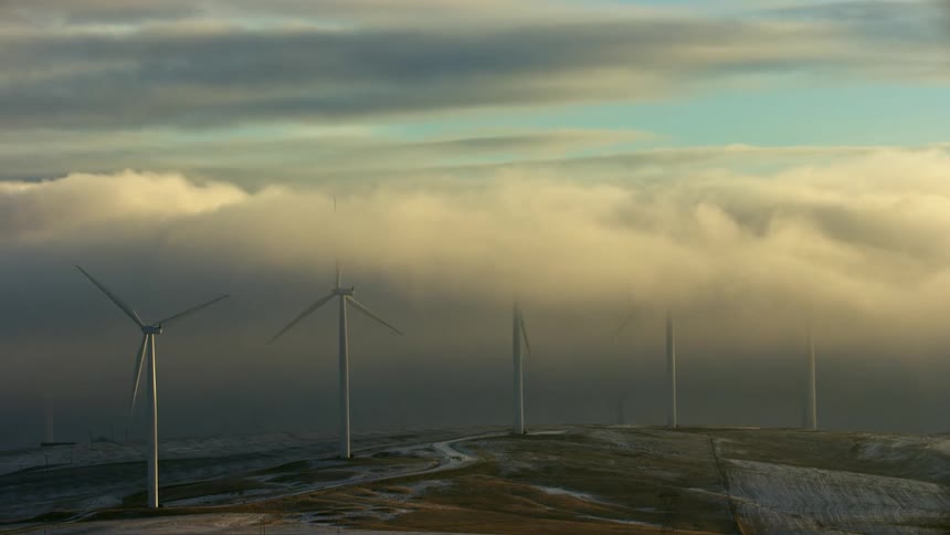 Fog at sunrise obscures some wind turbines and reveals others in this stunning renewable energy dynamic shot
