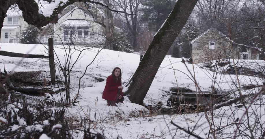 A woman kneels in the snow next to a tree