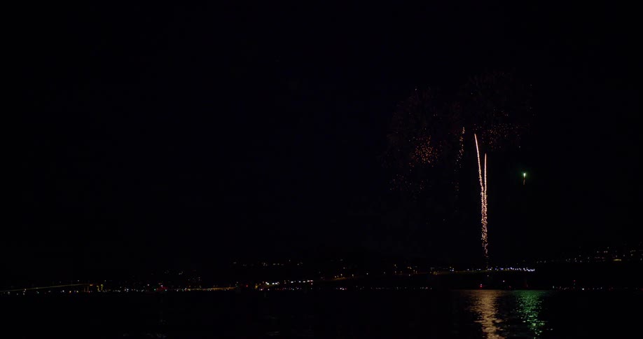 Fireworks light up the night sky from across a river near downtown