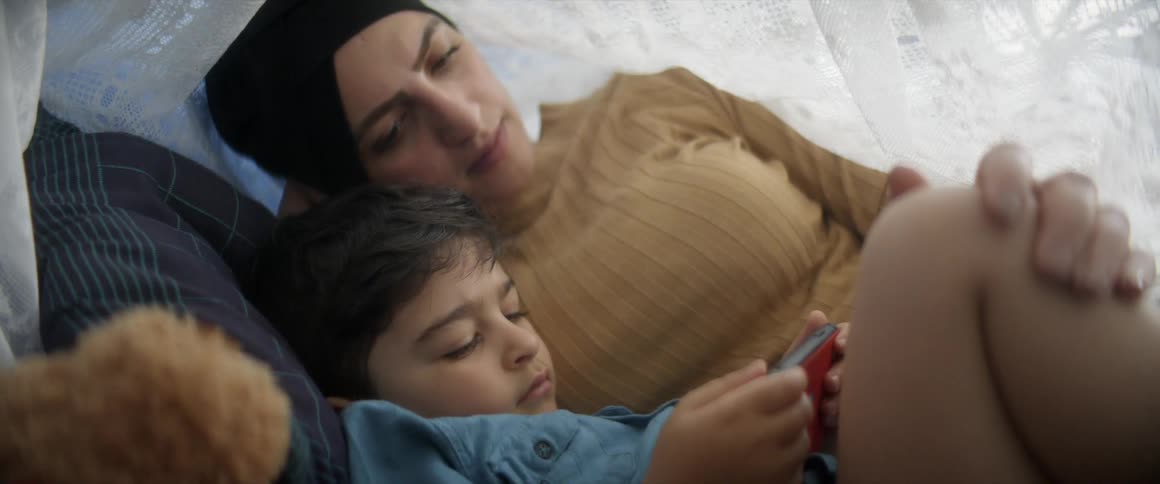 A woman lies in bed and watches her son play on a cell phone