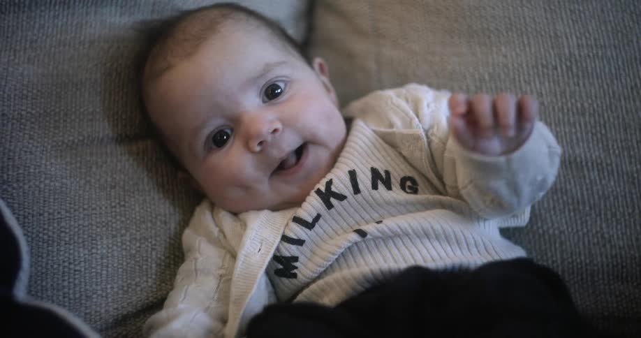 A baby is sitting on the couch waving her arms