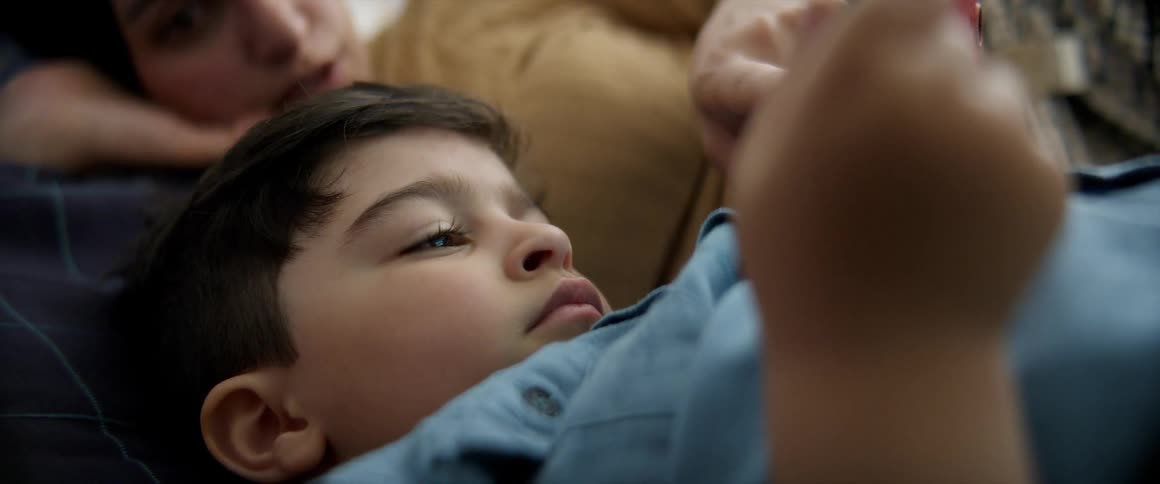 A boy and a woman are laying down and manipulating a device in the boys hands