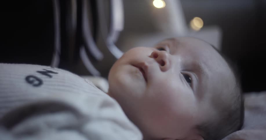A baby laying in bed at home looking up and moving her arms around