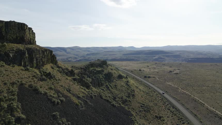 Traverse along desert cliffs and rugged rock formations as a car drives down an empty road that stretches to the horizon