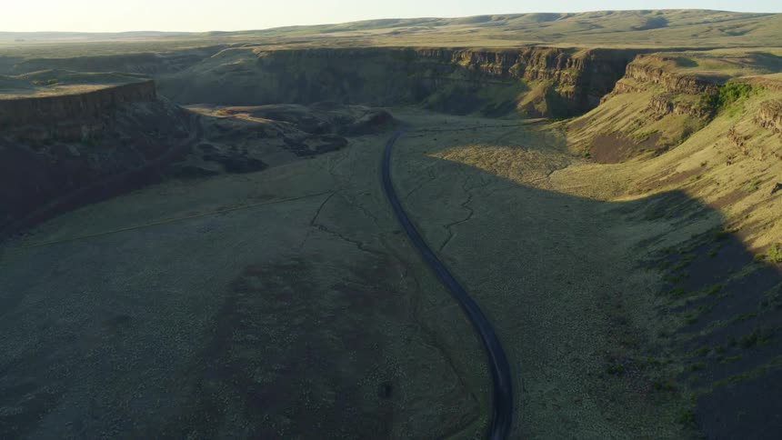 Tilt up from an empty and winding gravel road to reveal a desert canyon landscape