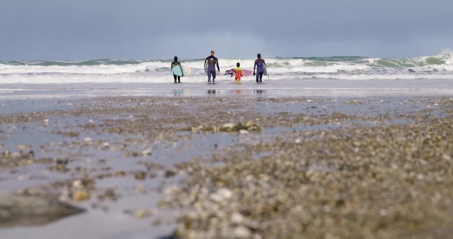 A surfer family walk towards coastal waves with surfboards