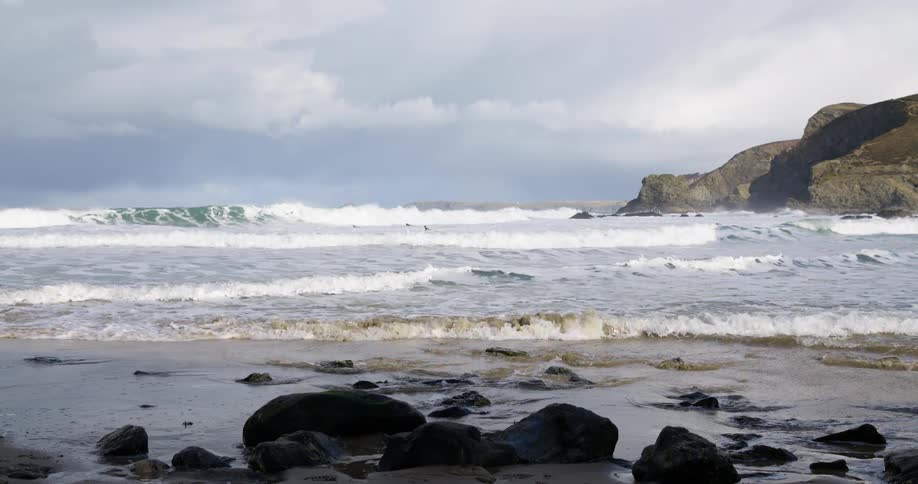 Waves roll in over a rock covered beach under a cloudy sky